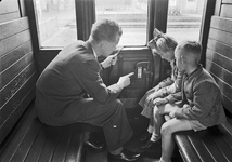 803551 Afbeelding van een vader met zijn twee kinderen in de coupé van een (houten) rijtuig van de N.S.